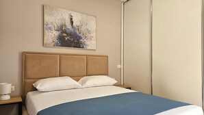 A bedroom with a bed, a nightstand, a lamp, and a painting on the wall. - Deep Blue Rooftop - 111 (Sarandë)