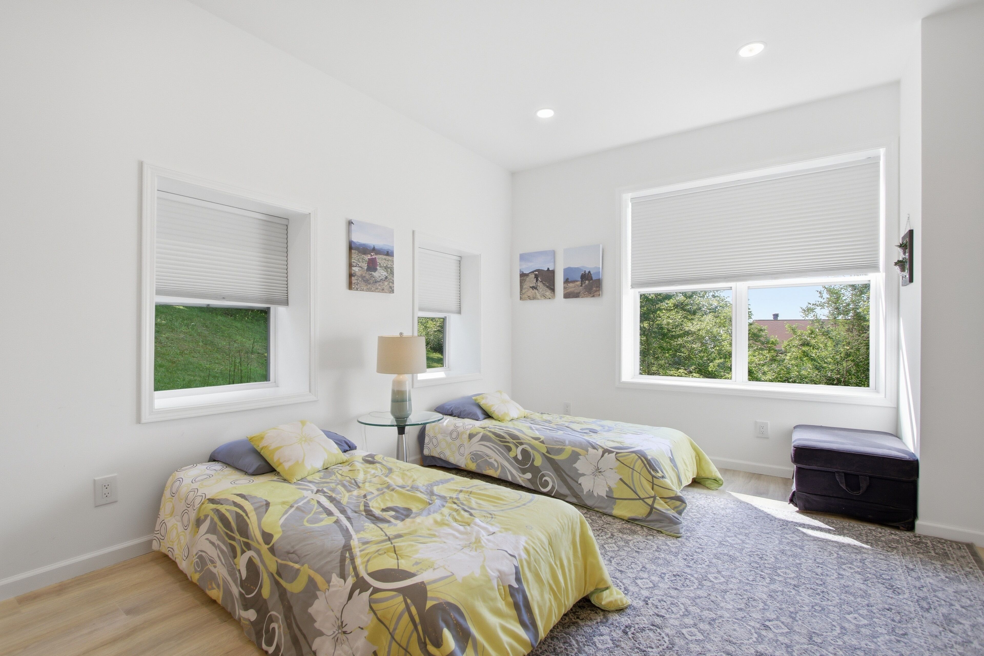 Quarto com duas camas, uma luminária e janela com persianas.