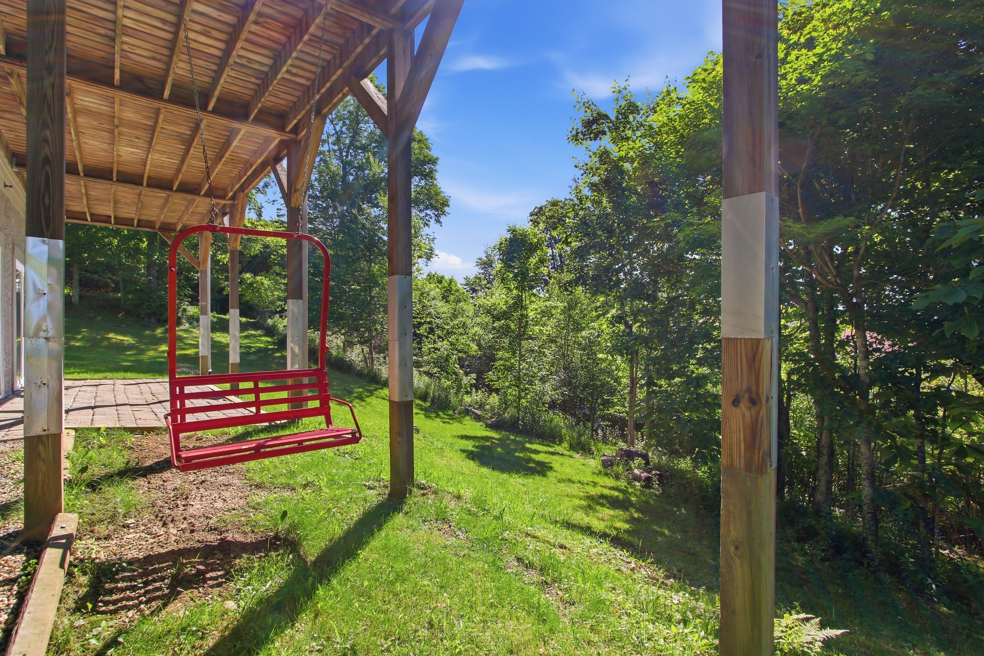 Une structure en bois abritée, dotée d’une balançoire, entourée de verdure et d’arbres.