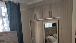 A neatly made bed with white linens, a bedside table, a mirror, and a wardrobe with a mirror. - Spacious 2br, 3BA Great Location (Nairobi)