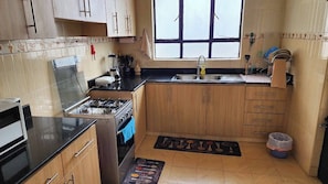 Une cuisine de taille réduite, équipée d’une cuisinière à gaz, d’un évier, de meubles de rangement en bois et d’une fenêtre.