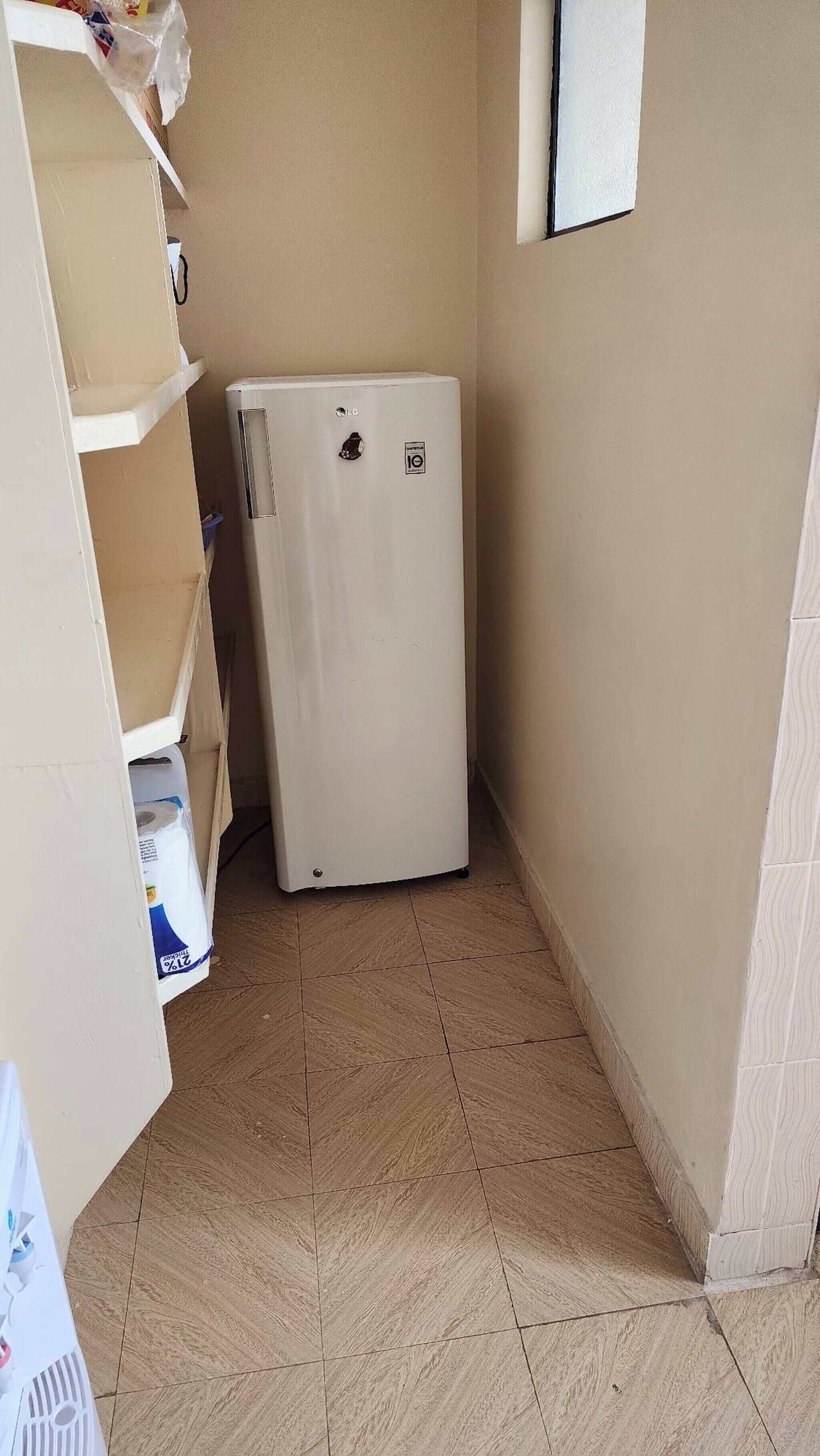 A small room with a white refrigerator, a tiled floor, and beige walls.
