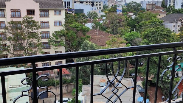 A balcony with a metal railing overlooking a cityscape with buildings and trees. - Spacious 2br, 3BA Great Location (Nairobi)