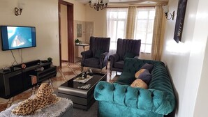 A living room with a television, two armchairs, a sofa, a coffee table, and a leopard print rug. - Spacious 2br, 3BA Great Location (Nairobi)