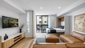 A modern hotel room with a bed, a leather sofa, a TV, and a balcony with a view. - Kove Apartment - G01 (Kiama)