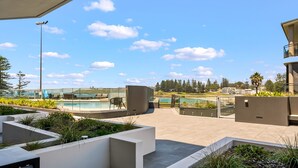 A modern outdoor pool area with glass barriers, seating, and a view of the ocean. - Kove Apartment - G01 (Kiama)