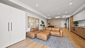 A modern living room with a sectional sofa, a dining area, and a kitchen with wooden cabinets. - Kove Apartment - G01 (Kiama)