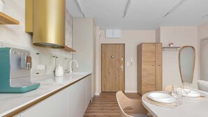 Una cocina moderna con armarios blancos, una cafetera azul turquesa y una mesa de comedor de madera para dos personas.