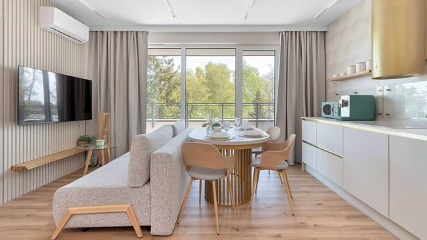 Una sala de estar moderna con sofá, mesa de comedor, sillas, televisión y cocina equipada con armarios y electrodomésticos.
