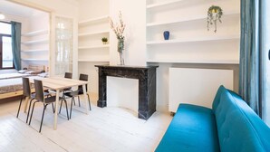 Een kamer met een bed, een eettafel met stoelen, een blauwe bank, een open haard en planken met planten.