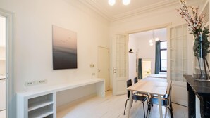 Een modern interieur met een witte bank, een eettafel met stoelen, een schilderij en een vaas met bloemen.