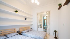 Een slaapkamer met twee bedden, een nachtkastje, een lamp, een plank met een plant, en een deur naar een badkamer.