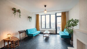 A modern living room with two blue sofas, a wooden coffee table, a small side table, and a fireplace. - 2BR Apartment Near Grand Central Station (Antwerp)