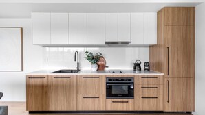 A modern kitchen with white upper cabinets, a wooden lower section, a stainless steel sink, and a built-in oven. - Kove Apartment - B01 (Kiama)