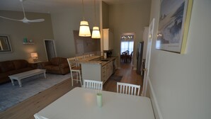Uma sala de estar com sofá, mesa de jantar com cadeiras, área de cozinha com armários e um ventilador de teto.
