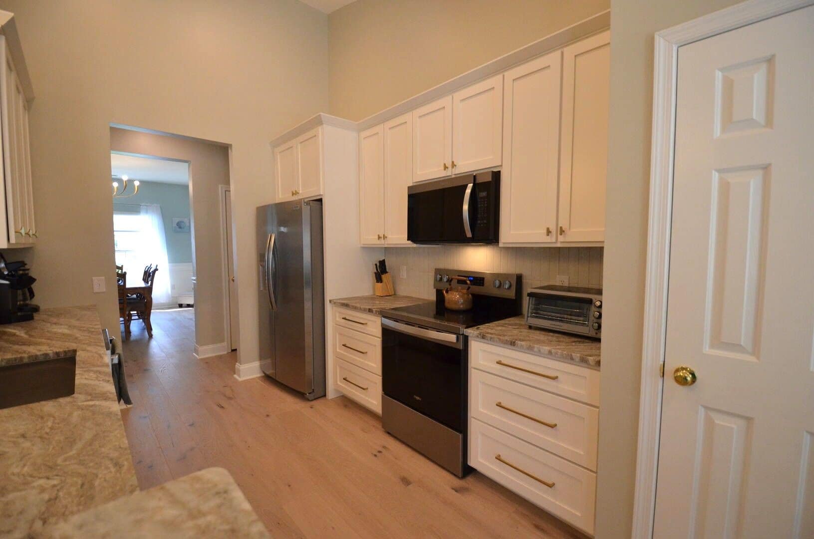 A kitchen with white cabinets, a stainless steel refrigerator, a microwave, a toaster oven, and a stove.