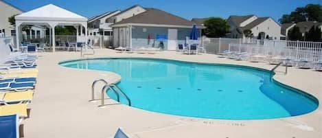 A swimming pool with lounge chairs and a covered area, surrounded by houses.