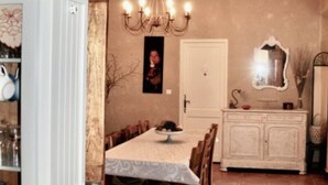 Un espace repas comprenant une longue table, des chaises, un lustre et un buffet blanc.