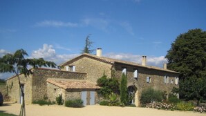 Un bâtiment en pierre avec un toit en tuiles, des fenêtres en arc de cercle et un jardin où poussent différentes plantes et fleurs.
