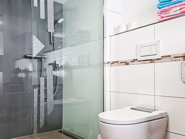 A modern bathroom with a glass shower enclosure, a white toilet, and a towel rack with folded towels.