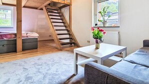 Et værelse med køjeseng, et lille bord med en vase, et vindue med udsigt og en grå sofa.