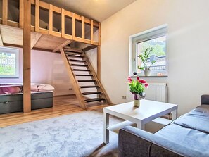 Ein Zimmer mit einem Etagenbett, einem kleinen Tisch mit einer Vase, einem Fenster mit Aussicht und einem grauen Sofa.