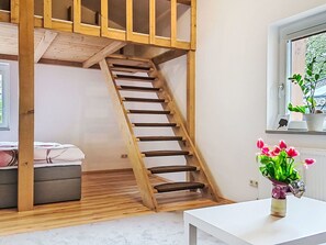 Eine Holztreppe in einem Zimmer mit einem Bett, einem weißen Tisch und einem Fenster mit einer Pflanze.