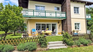Un edificio su due piani con un balcone, un piccolo giardino e un tavolo apparecchiato all'esterno.