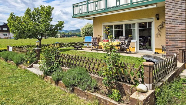 Una casa a due piani con un balcone, un patio con mobili da esterno e un giardino recintato.