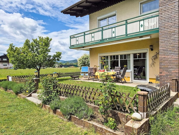A two-story house with a balcony, a patio with outdoor furniture, and a fenced garden area.