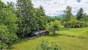 Un parco erboso con alberi, una piccola costruzione in legno e un muro di pietra.