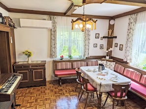 A dining area with a wooden table, chairs, a bench, a piano, and a window with curtains.