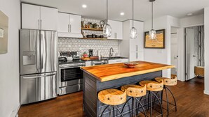 Eine moderne Küche mit Edelstahlgeräten, einer Holztischinsel mit Barhocker, Pendelleuchten und einer sechseckigen Fliesenspiegel.