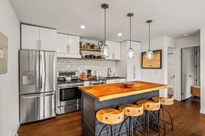 A modern kitchen with stainless steel appliances, a wooden island with bar stools, pendant lighting, and a hexagonal tile backsplash. - Chic Mountain Condo w/Beautiful Mtn Views (Steamboat Springs)