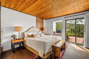 A bedroom with a wooden ceiling, a large bed with a headboard, two bedside tables, a bench, and a view through a sliding glass door to an outdoor area. - Chic Mountain Condo w/Beautiful Mtn Views (Steamboat Springs)