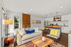 A modern living room with a sofa, coffee table, and a kitchen area with a dining table and bar. - Chic Mountain Condo w/Beautiful Mtn Views (Steamboat Springs)