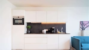 Eine moderne Küche mit weißen Schränken, einem Bosch-Ofen, einer Kaffeemaschine und einem blauen Sofa im Wohnbereich.