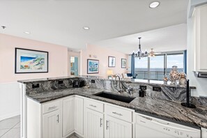 A kitchen with a granite countertop, white cabinets, a black sink, and a view of the ocean through large windows. - 🏖️ Santa Rosa Towers 1402 | 3BR Pensacola Beach | Pool, Tennis & Gulf Views (Pensacola Beach)