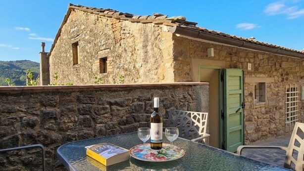 Un bâtiment en pierre avec une porte verte, une table avec une bouteille de vin et des verres, et un livre.