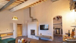 Ein Wohnzimmer mit grünen Sofas, einem Kamin, einem Fernseher und einer Küchenzeile mit einer Weinflasche und Gläsern.