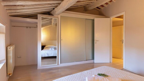 Ein Schlafzimmer mit einem Bett, einem Heizkörper, einer Holzbalkendecke und einer Tür zu einem weiteren Raum.