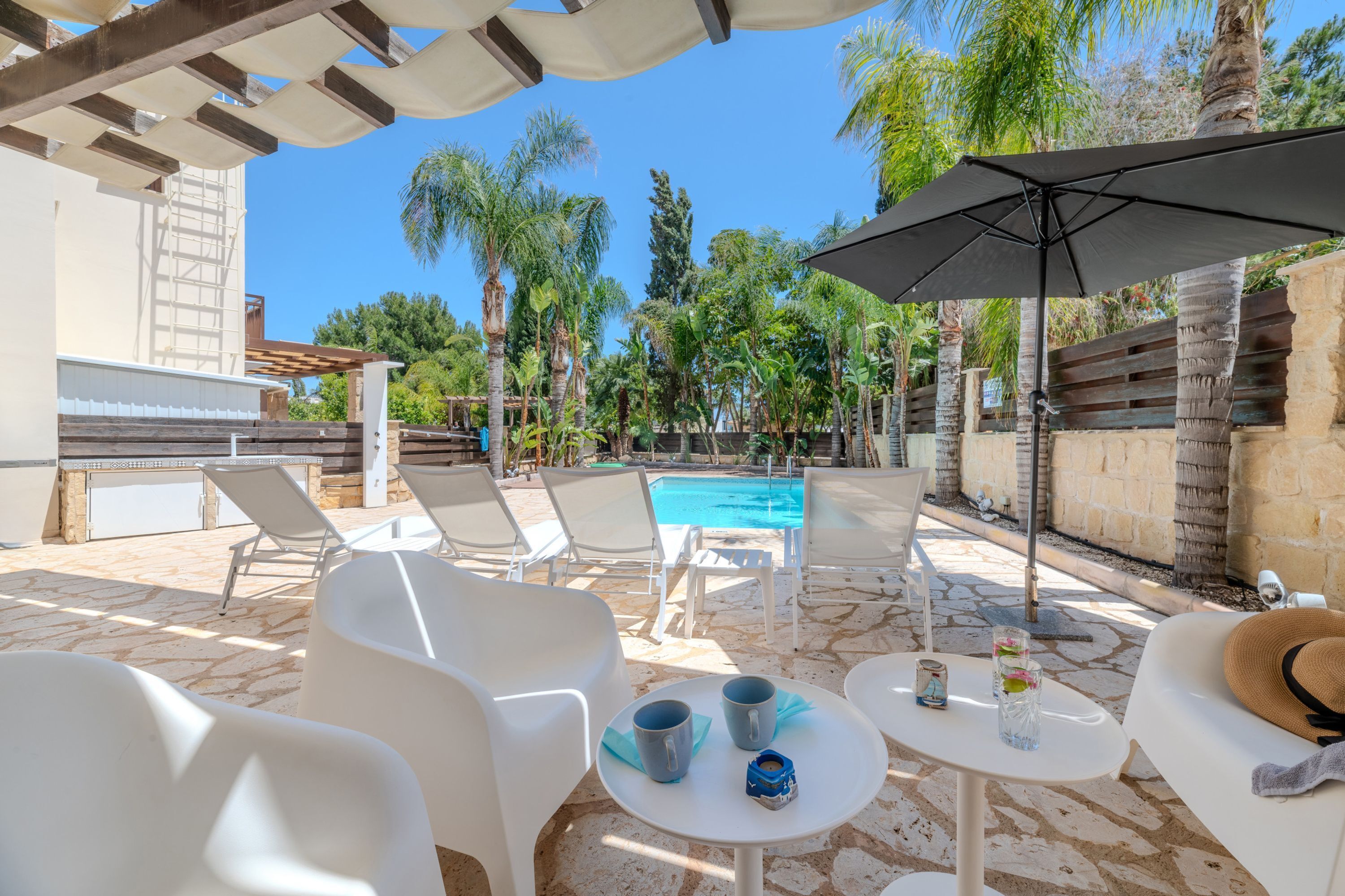 Un espace aménagé au bord de la piscine, avec des chaises longues blanches, une table avec des boissons et un grand parasol.