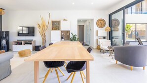 Een moderne woonruimte met een houten eettafel, zwarte stoelen, een grijze bank, een televisietoestel en een groot raam.
