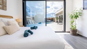 Een moderne hotelkamer met een groot bed, een glazen schuifdeur naar een zwembad en een potplant.