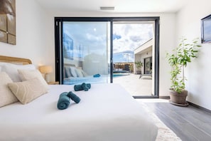 Una habitación de hotel moderna con una cama grande, un ventanal corredero que da a una zona de piscina y una planta en maceta.