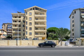 Edifício residencial com vários andares, varandas, área de estacionamento e céu claro.