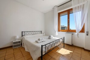 A bedroom with a bed, a nightstand, a window with curtains, and a radiator.