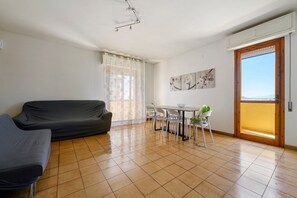 Un salon comprenant un canapé, une table à manger avec des chaises, une fenêtre avec des rideaux et une porte donnant sur un balcon extérieur.