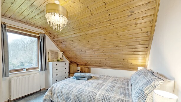 A bedroom with a sloped ceiling, a bed with a plaid bedspread, a dresser, a chair, and a window with curtains. - Ancton Way by the Sea - sleeps 9 guests  in 4 bedrooms (Bognor Regis)