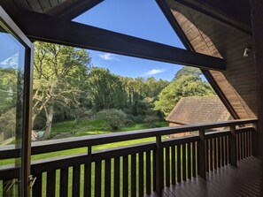 En träveranda med utsikt över ett grönskande landskap och en byggnad med ett tak täckt av tegelpannor.